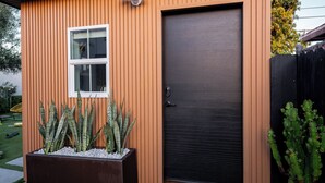 Ett modernt hus med en mörk dörr, ett fönster och en blomkruka med kaktusar.