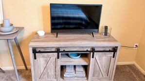 En tv-apparat står på ett TV-bord i trä, bredvid ligger en fjärrkontroll och ett glas vatten.