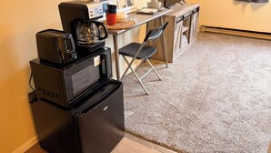 Ett litet pentry med en kaffebryggare, brödrost och mikrovågsugn. Det finns ett litet kylskåp, en hopfällbar stol och ett matbord med några få föremål på.