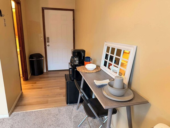 A compact kitchen with a coffee maker, a microwave, and a small table with a bowl and a cup.