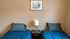 A hotel room with two single beds, each with a blue duvet, a bedside table with a lamp, and a framed picture on the wall. - NDSU Efficiency (APT 3) (Fargo)