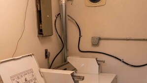 A compact laundry area with a front-loading washer and dryer, a wall-mounted exhaust fan, and visible electrical outlets. - Cozy Studio Near NDSU (Apt 5) (Fargo)