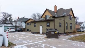 A two-story residential building with a garage, a driveway with snow, and a dumpster in the foreground. - Cozy Studio Near NDSU (Apt 5) (Fargo)