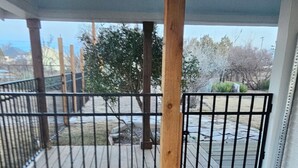 Una terraza de madera con una reja metálica, postes de madera y vistas a una zona ajardinada con árboles y un sendero de piedra.