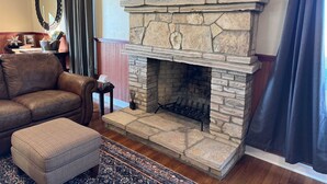 Una sala de estar acogedora con chimenea de piedra, sofá de cuero, reposapiés y alfombra estampada.