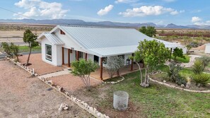Una casa de un piso con techo de metal, rodeada de un pequeño jardín y una vista despejada de montañas lejanas.