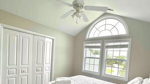 Ein Schlafzimmer mit Bett, Deckenventilator, großem Fenster und weißen Türen.