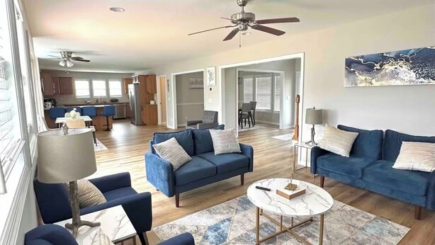 Ein geräumiges Wohnzimmer mit blauen Sofas, einem Couchtisch und einem Deckenventilator.