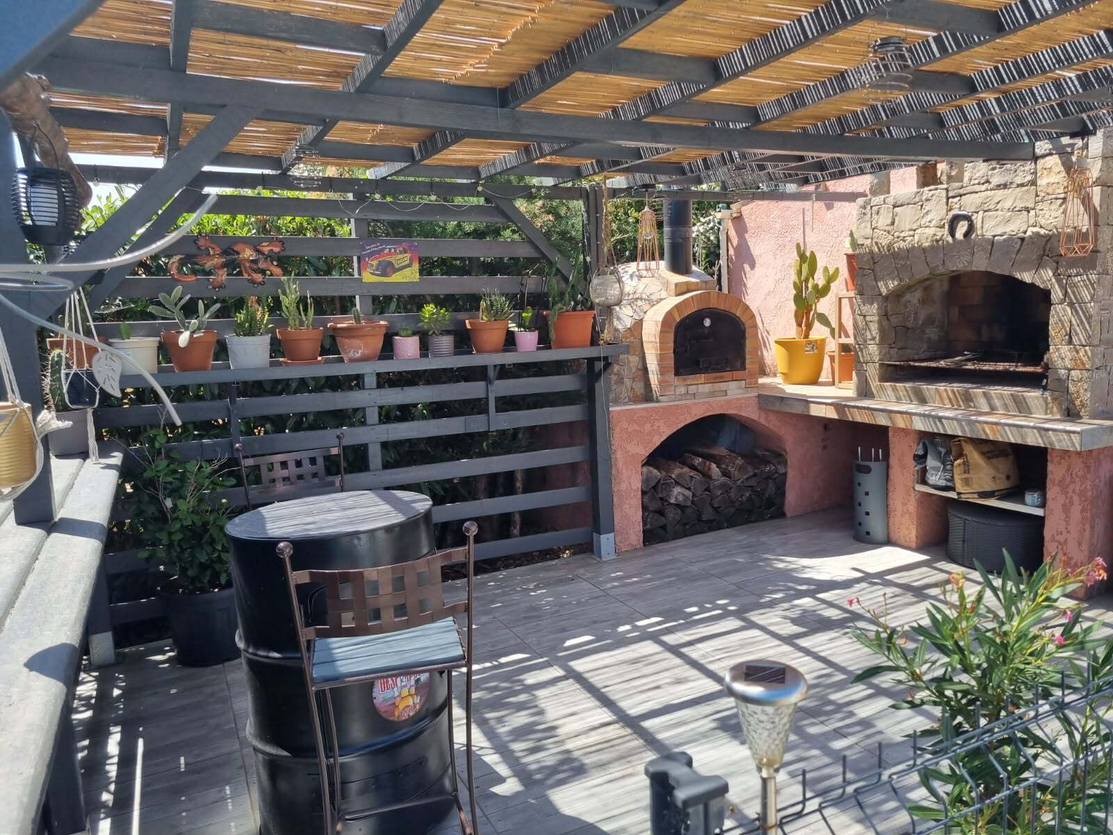Un patio al aire libre con un horno de pizza de piedra, una parrilla y diversas plantas en macetas.