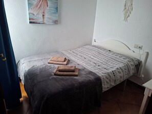 Ein Schlafzimmer mit einem Bett, zwei Handtüchern, einer gemusterten Tagesdecke, einem Bild an der Wand und einem weißen Nachttisch.