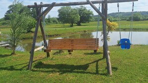 A wooden swing set with a bench in a grassy area near a body of water. - Romantic vacation apartment with large garden - 2 min. from private natural swimming lake (Kerkateskánd)