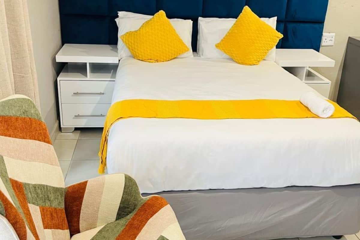 Ein Hotelzimmer mit einem großen Bett, zwei Nachttischen, einem Sessel und einem blauen Kopfteil.