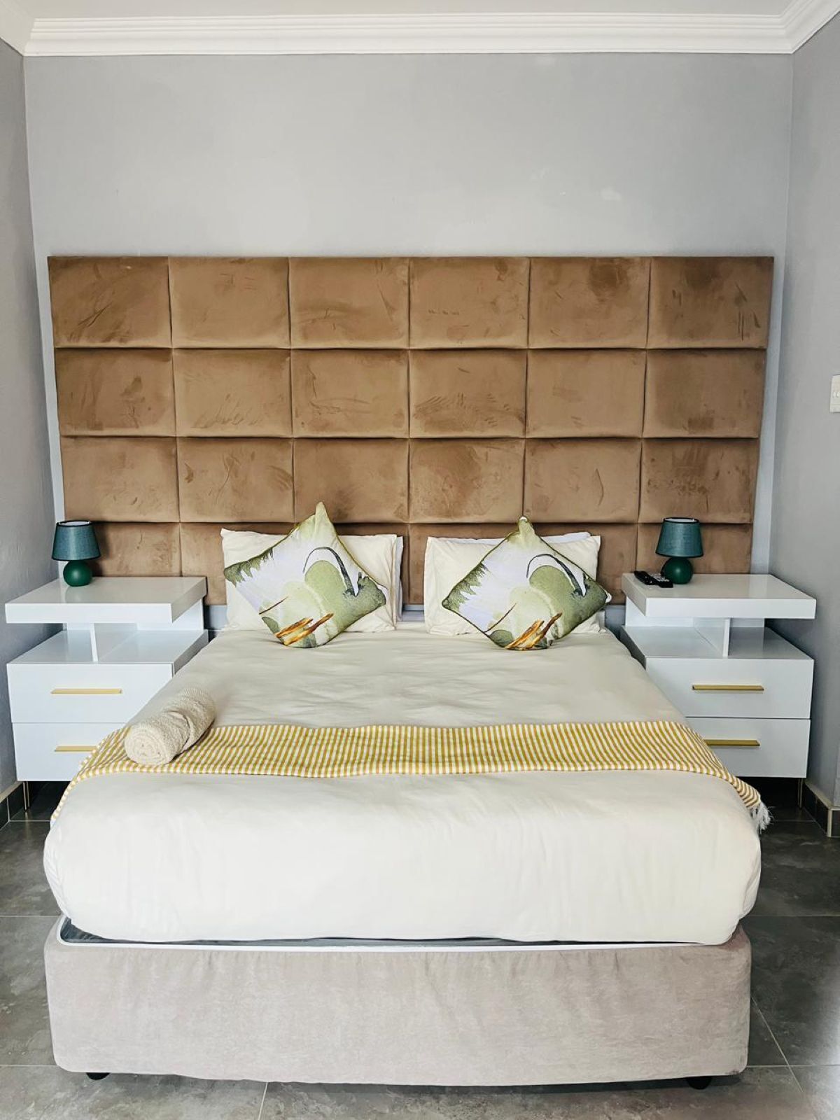 A bedroom with a tufted headboard, a bed with white bedding, two bedside tables with lamps, and a striped throw blanket.
