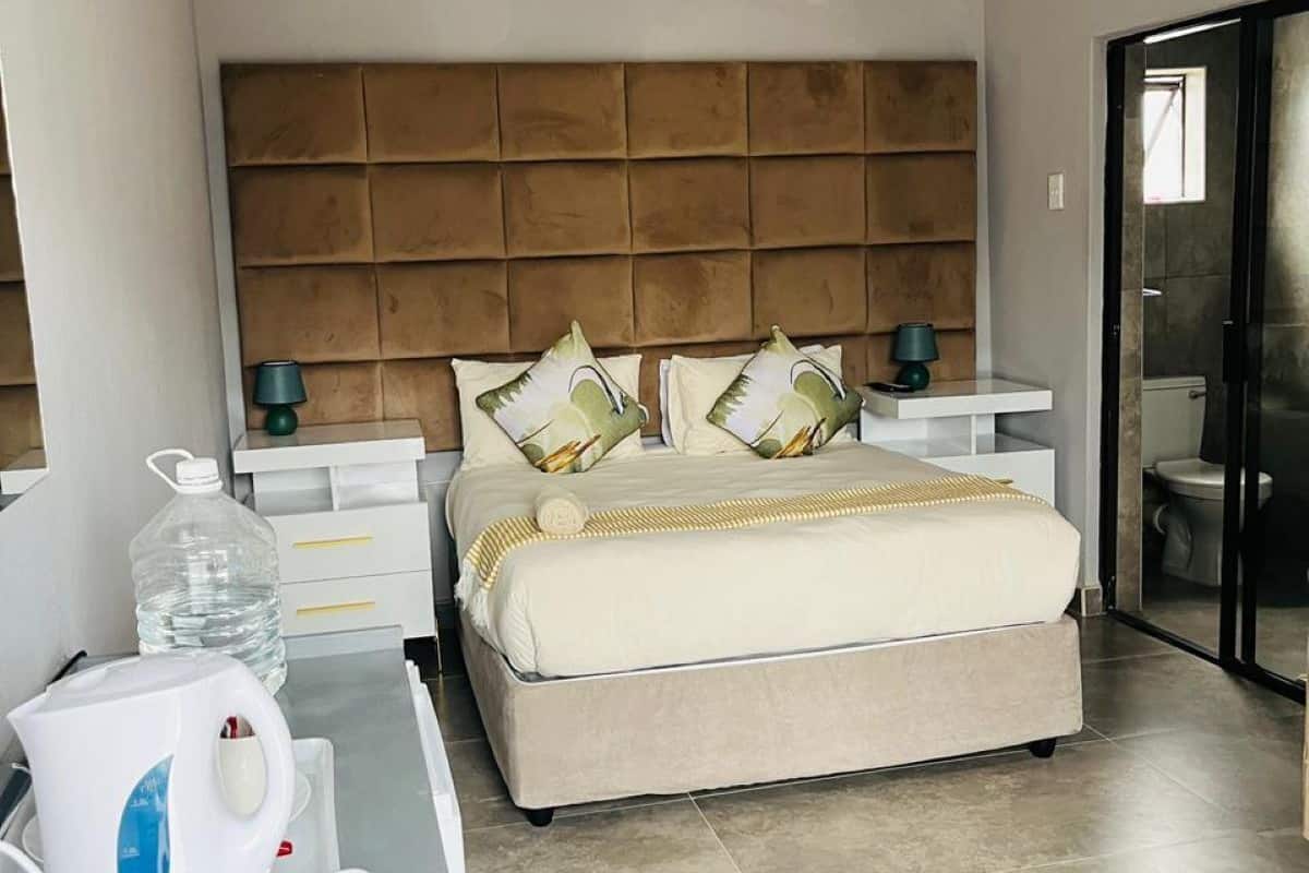 Ein modernes Schlafzimmer mit einem großen Bett, einem Kopfteil, Nachttischen und Blick ins Badezimmer durch eine Glastür.