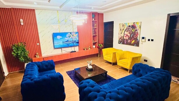Uma sala de estar moderna com uma televisão de tela plana grande, uma poltrona amarela e um sofá azul.