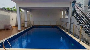 A rectangular swimming pool with a wooden deck surrounding it, a metal railing, and a staircase leading to an upper level. - Luxury 4BR Retreat (Lekki)