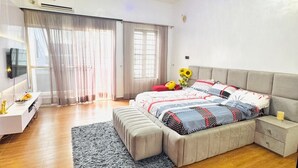 Quarto moderno com uma cama grande, mesa de cabeceira, televisão e janela com cortinas.