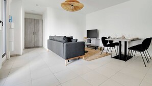 A modern living room with a grey sofa, a dining table with black chairs, a TV, and a unique ceiling light. - Elegant Appt - 1BDR/4P - Near Paris & La Défense (Suresnes)