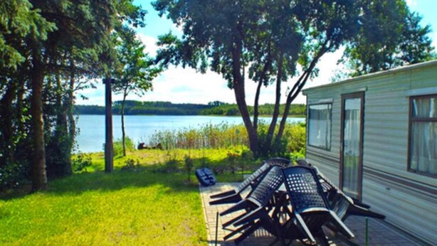 A campsite with a table and chairs, a grassy area, and a lake view. - Mobile Home im Ferienpark mit Seezugang (Dabel)
