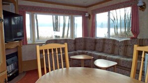A living room with a sofa, two small tables, a television, and a window with a view of a lake. - Mobile Home im Ferienpark mit Seezugang (Dabel)