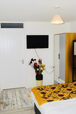 A bedroom with a bed, a TV mounted on the wall, a mirror, and a vase with flowers. - Stylish & Compact Central MK 1-Bed Walk to Station | Business Ready Free Parking (Oldbrook)