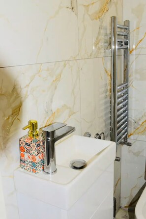 A bathroom with a marble wall, a sink with a chrome faucet, and a towel rack. - Stylish & Compact Central MK 1-Bed Walk to Station | Business Ready Free Parking (Oldbrook)