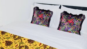 En säng med vita lakan och två kuddar med färgglada blommönster.