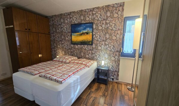 Un dormitorio con cama, mesita de noche, lámpara, armario y un cuadro en la pared.