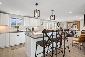Una cocina moderna con armarios blancos, una isla central y taburetes de bar.