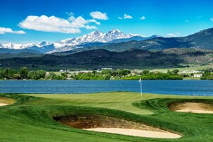 Un campo de golf con una bandera, un lago y montañas al fondo.