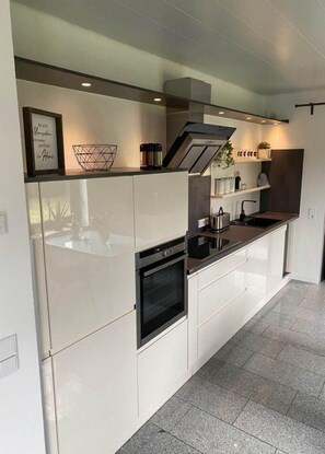 Une cuisine moderne avec des meubles blancs, un four encastré et une hotte de cuisson en acier inoxydable.