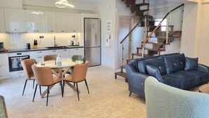 A modern kitchen with white cabinets, a dining area with a table and chairs, and a staircase leading to another level.