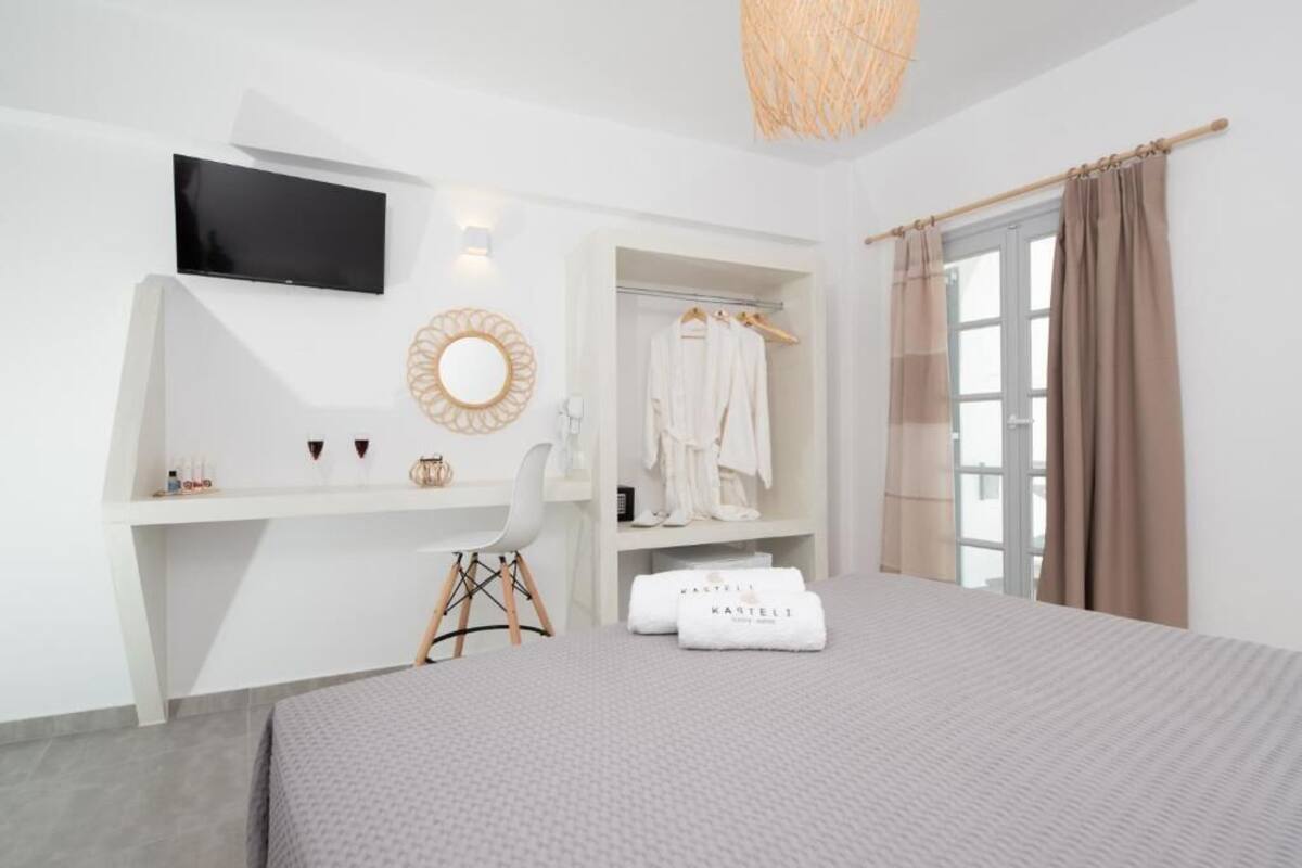 Een moderne slaapkamer met een bed, een aan de muur bevestigde televisie, een bureau met stoel, een kledingkast en een raam met gordijnen.