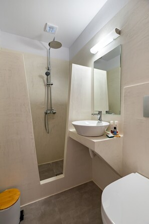 A bathroom with a shower, sink, toilet, and a mirror. - Kasteli Luxury Rooms (Perissa)