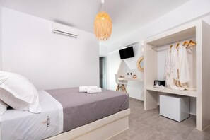 A modern bedroom with a bed, a wardrobe, a desk, and a hanging light fixture. - Kasteli Luxury Rooms (Perissa)