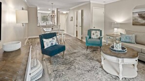 Un salon spacieux avec un fauteuil bleu, un fauteuil turquoise, une table basse blanche et un tapis gris.