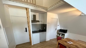 Ett kompakt kök med mikrovågsugn, diskho och ett litet kylskåp. Där finns ett matbord i trä med två röda stolar.