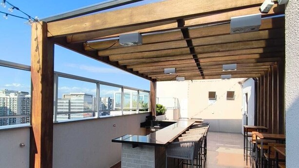 Une terrasse sur le toit agrémentée d’une pergola en bois, d’un bar central et de plusieurs espaces aménagés pour s’asseoir.