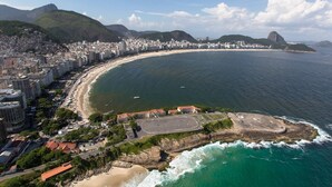 An aerial view of a coastal city with a long beach, dense urban area, and mountains in the background.
