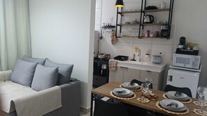 Un espace de vie compact comprenant un canapé, une table à manger, des chaises, un coin cuisine avec un four à micro-ondes et un luminaire suspendu.
