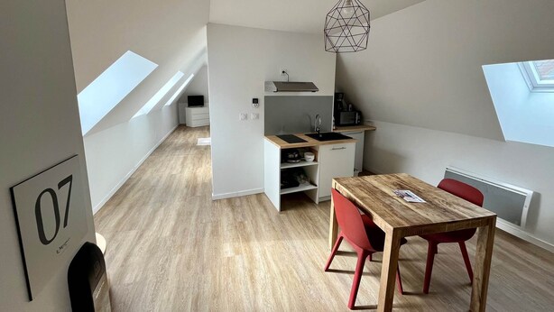 A modern apartment with a dining area, kitchenette, and a loft bedroom with skylights.