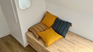 A corner of a room with a wooden bench, two pillows, and a wall-mounted mirror.