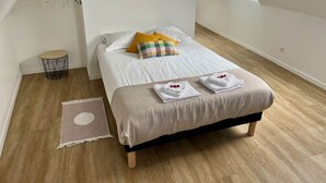 A bedroom with a bed, a small round table, a wall-mounted rack, and a window.