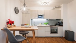 Una cocina compacta con microondas, horno y cafetera. Hay una mesa de madera con un cuenco de fruta y una planta en maceta.