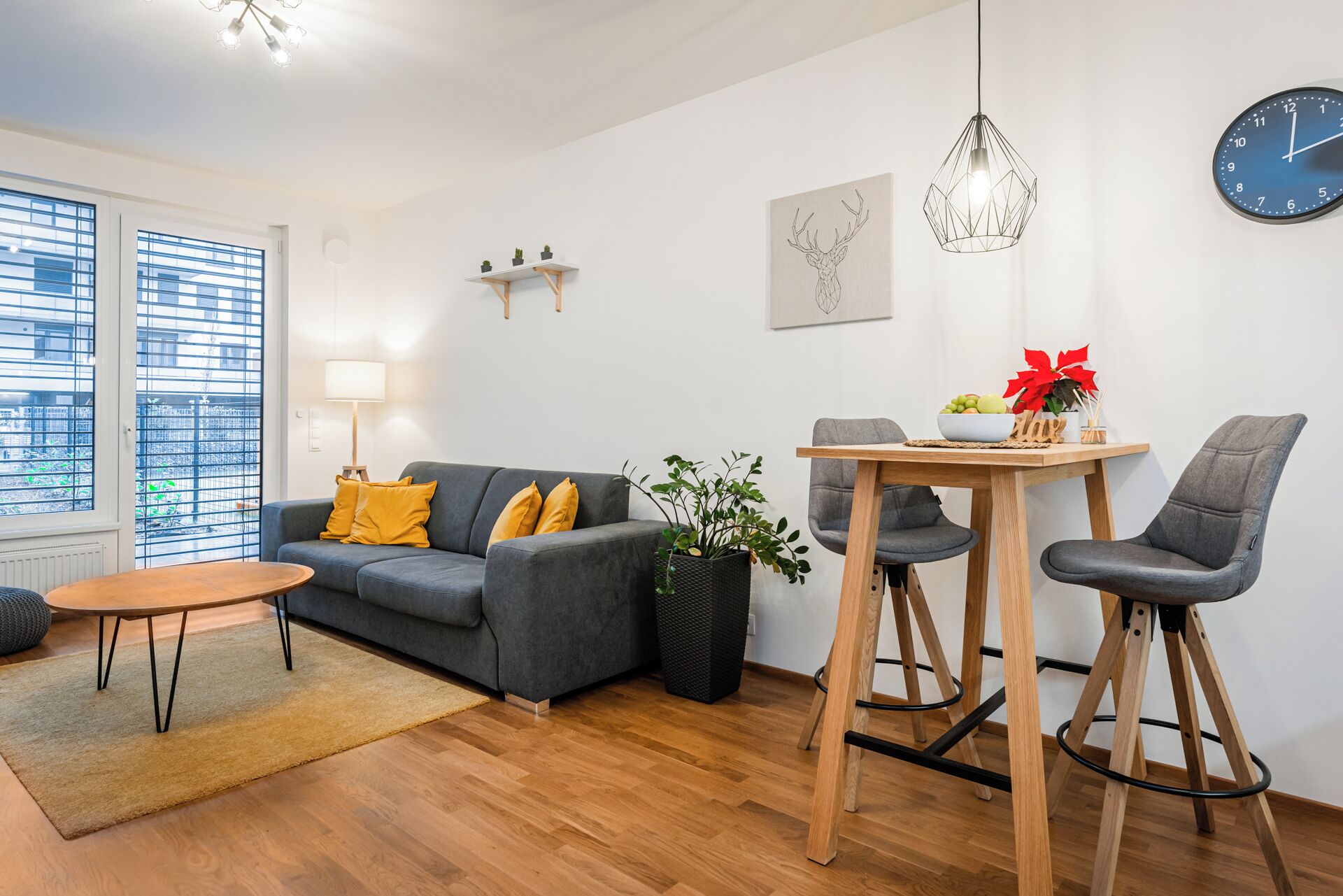 A modern living room with a grey sofa, a wooden coffee table, and two bar stools.
