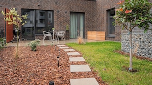 Un edificio moderno de ladrillo con un patio que cuenta con una parrilla, mobiliario exterior y un sendero en el jardín.