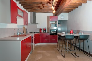 A kitchen with red cabinets, a stove, an oven, and bar stools.