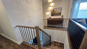 A staircase with wooden railings and a view of a living area with a sofa and a painting on the wall. - Close to Wineries, The Beach, trails, and Downtown (Penticton)