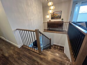 A staircase with wooden railings and a view of a living area with a sofa and a painting on the wall. - Close to Wineries, The Beach, trails, and Downtown (Penticton)