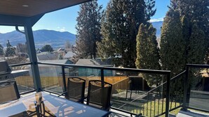 A balcony with a glass railing, outdoor furniture, and a view of a mountainous landscape. - Close to Wineries, The Beach, trails, and Downtown (Penticton)